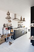 Shelves on castors and retro bar stool next to modern kitchen counter below industrial-style pendant lamps in rustic interior