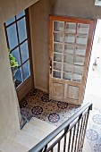 Blick von Treppe in Diele mit gemusterten Fliesenboden, offene Haustür aus abgelaugtem, hellem Holz
