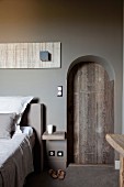 Arched doorway with rustic wooden door in grey-painted wall of elegant bedroom