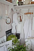 White rustic clothing hung on clothes hangers on white-stained wooden wall