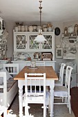 Rustic dining table and white wooden chairs in front of dresser in cosy kitchen-dining room
