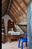 Blick durch offene Tür auf blauen Schaumstoff-Stuhl in rustikalem Schlafzimmer unter dem Dach