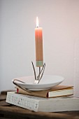 Lit candle on candlestick made from bent vintage fork and saucer on stack of books
