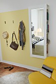 Useful hooks on pale yellow wall panel next to mirror with concealed storage space in bedroom