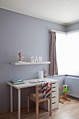 Schlichter Schreibtisch in Weiß und Holzstuhl vor grauer Wand im Kinderzimmer