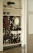 Wardrobe integrated into niche with floral black and white wallpaper and glass ornaments on shelves