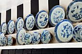 Collection of blue and white plates and bowls on wooden shelves on wallpaper with wide stripes