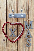 Weihnachtliche Wanddekoration mit Herz aus Cranberries & Schriftzug XMAS aufgehängt an Garderobenhaken