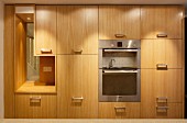 Kitchen cupboards with wooden fronts and stainless steel handles, fitted appliances and integrated aperture with view of staircase