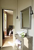 Curved, grey washstand with basin below framed mirror on wall with bedroom seen through open door in background