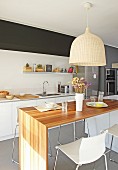 Pendant lamp with wicker lampshade above dining table and bar stools in open-plan designer kitchen