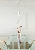 Branch of cotton bolls in sand-filled vases on designer glass table, classic chair and modern, white artwork on wall