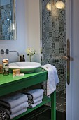 Green-painted washstand with countertop sink next to shower area with black and white patterned wall tiles