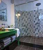 Green-painted washstand with countertop sink next to shower area with black and white patterned wall tiles