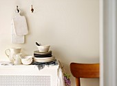 White wooden chopping boards hanging on white wall above stacked crockery and white jugs