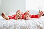 Siblings wearing red pyjamas lying on bed