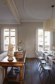 Bulky, antique console table, festively set dining table and classic chairs in period building with stucco ceiling