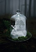Stag ornament on artificial snow and hand-stamped card with Christmas motif under glass cover on pewter plate with moss and fern fronds