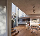 Offener Wohnraum mit Sichtbetondecke, Essplatz mit Klassikerstühlen, im Hintergrund Einbauküche, in zeitgenössischer Architektur