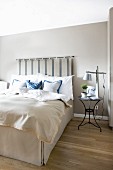 Box-spring bed with pale valance and bedspread and upholstered headboard hung on wall painted pale grey in elegant bedroom