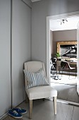 Chair with pale upholstery between open interior door and fitted cupboard