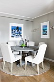 Dining area in corner of pale grey room with white upholstered chairs around round table on sisal rug