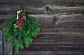 Green fir branches and hand-crafted felt fir cone hanging on rustic wooden wall
