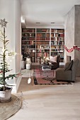 Elongated, festively decorated living room with bookcase and seating area in front of fireplace