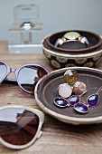 Sunglasses and jewellery in ceramic bowls on wooden table