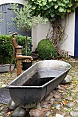 Vintage zinc bathtub next to pump in cobbled courtyard
