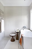 Zweiteiliges Beistelltischset aus Holz, neben freistehender weißer Badewanne am Fenster in modernem Bad mit Vintage Flair