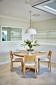 Round wooden table and chairs below pendant lamp with white lampshade in dining room