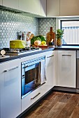 White kitchen with L-shaped counter, gas hob and splashback with fish-scale pattern