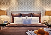 Kissen auf Doppelbett mit Polster Kopfteil an tapezierter Wand mit beigefarbenem Retro Muster