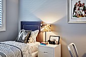 Table lamp on bedside table and single bed with leather-covered headboaard