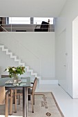 Essplatz mit modernem Tisch mit Glasplatte, im Hintergrund Treppenaufgang mit minimalistischem Geländer
