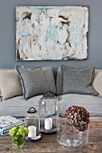 Sofa below modern artwork, candle lanterns and dried hydrangea flower on wooden table