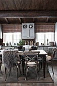 Rustic wooden chairs, some with animal-skin blankets, around dining table in rustic dining room of wooden house