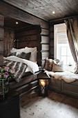 Lit candle in floor lantern next to cubby bed with fur blanket and window seat in wooden house