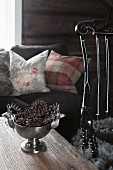 Silver bowl of pine cones on wooden table in front of sofa with scatter cushions