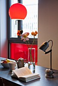 Vintage metal table lamp and open book below pendant lamp with red spherical lampshade