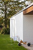 Outdoor shower and push-along tricycle in front of whitewashed brick wall in summery garden