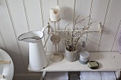 Enamel jug, candlestick and flowering branches in ceramic beaker on old wooden bench in shabby-chic bathroom