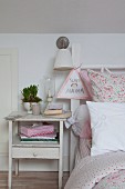 Shabby-chic bedside cabinet next to bed with floral bed linen and child's drawing hung from bedstead