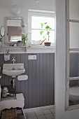 Small bathroom with grey wooden wainscoting and old window used as shower screen