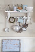 Vintage kitchen utensils hanging from hooks below bracket shelf and sky-blue, shabby-chic tray leaning against wainscoting
