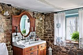 Solid wooden washstand with mirror in corner of rustic bathroom with stone walls