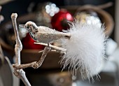 Ornamental metal bird with tail made from white feathers clipped to branch