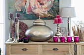 Metal pot with lid, candles in silver candlesticks and tealight holders on wooden lowboy