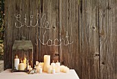 Lit candles on table and in lantern below Christmas greeting on board wall